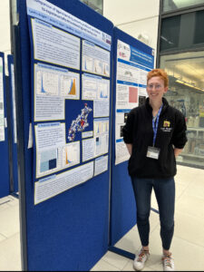 Photograph of Caitlin Wright stood next to a noticeboard.